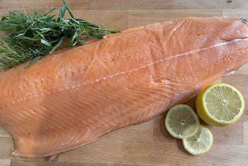 side of salmon on a board with a bunch of tarragon and lemon.