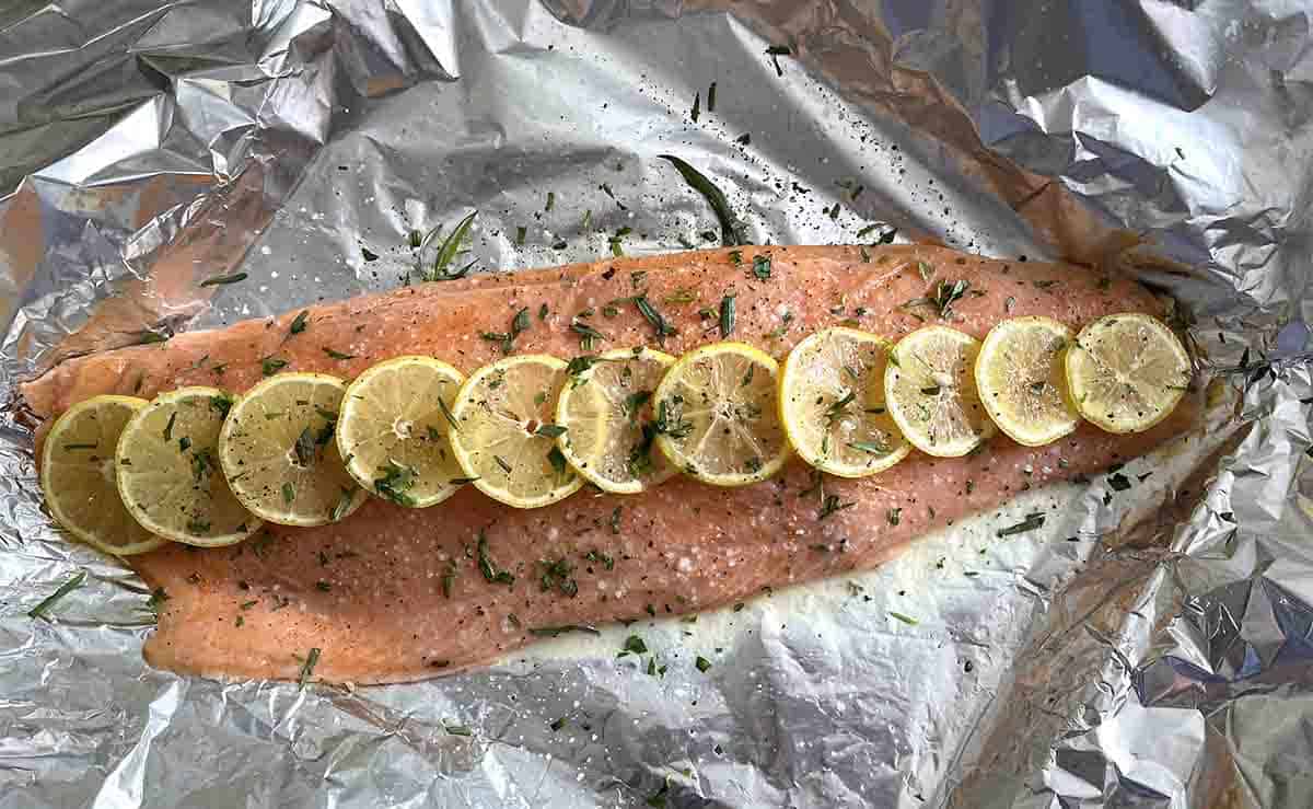 piece of salmon on foil wuth sliced lemon on top.