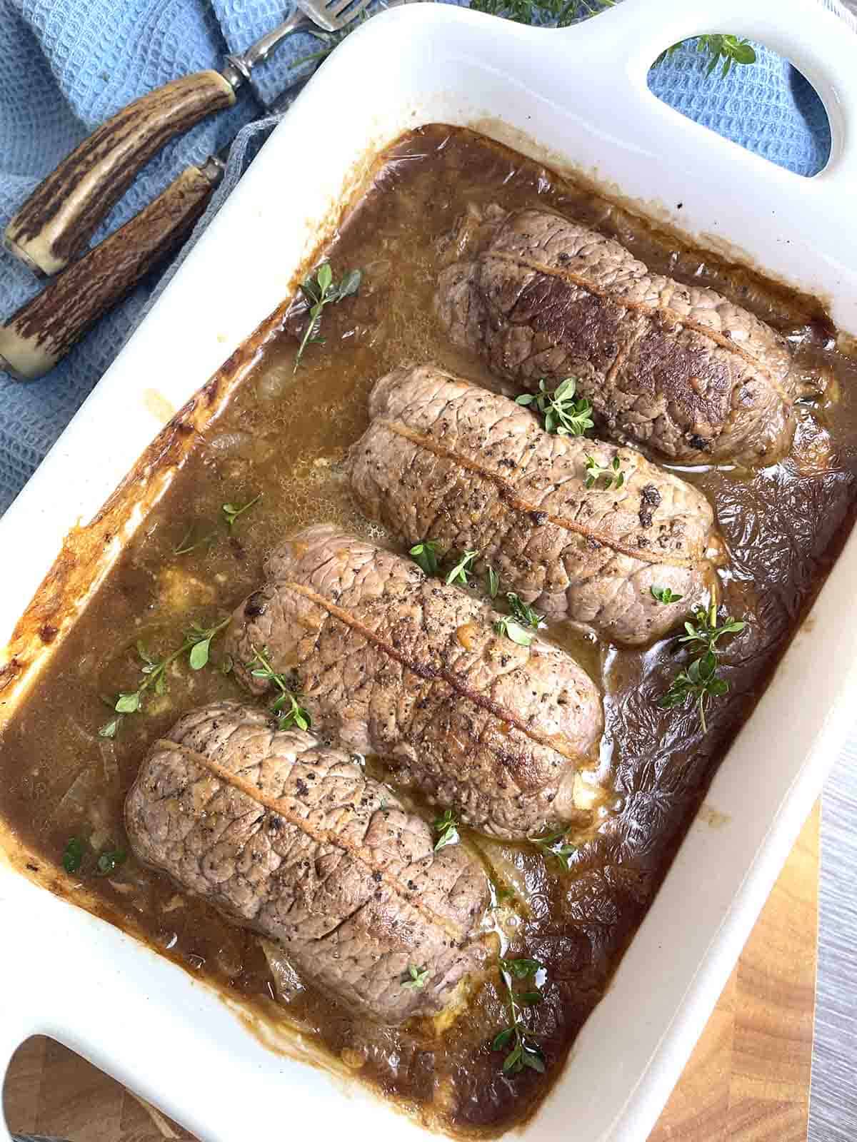 Beef olives in brown sauce in a serving dish.
