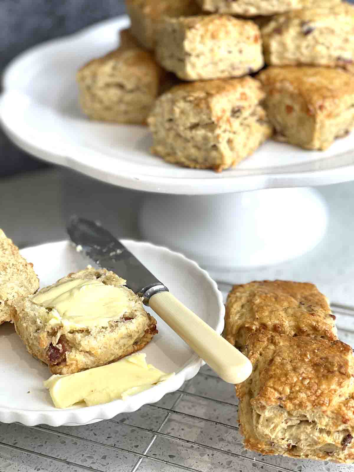 close up of buttered cut scone on a plate surrounded by scones.