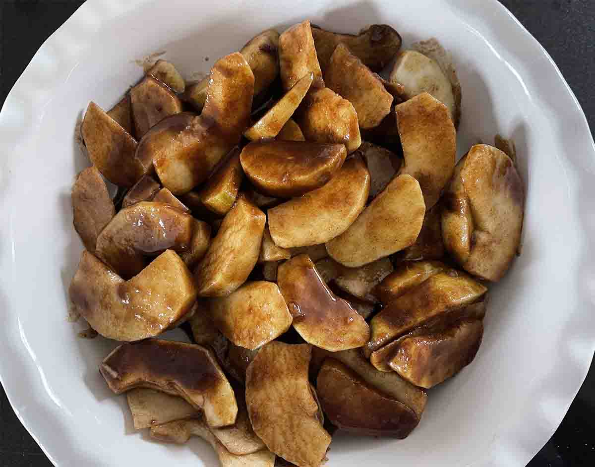 apples in a bowl mixed with dark brown sugar.