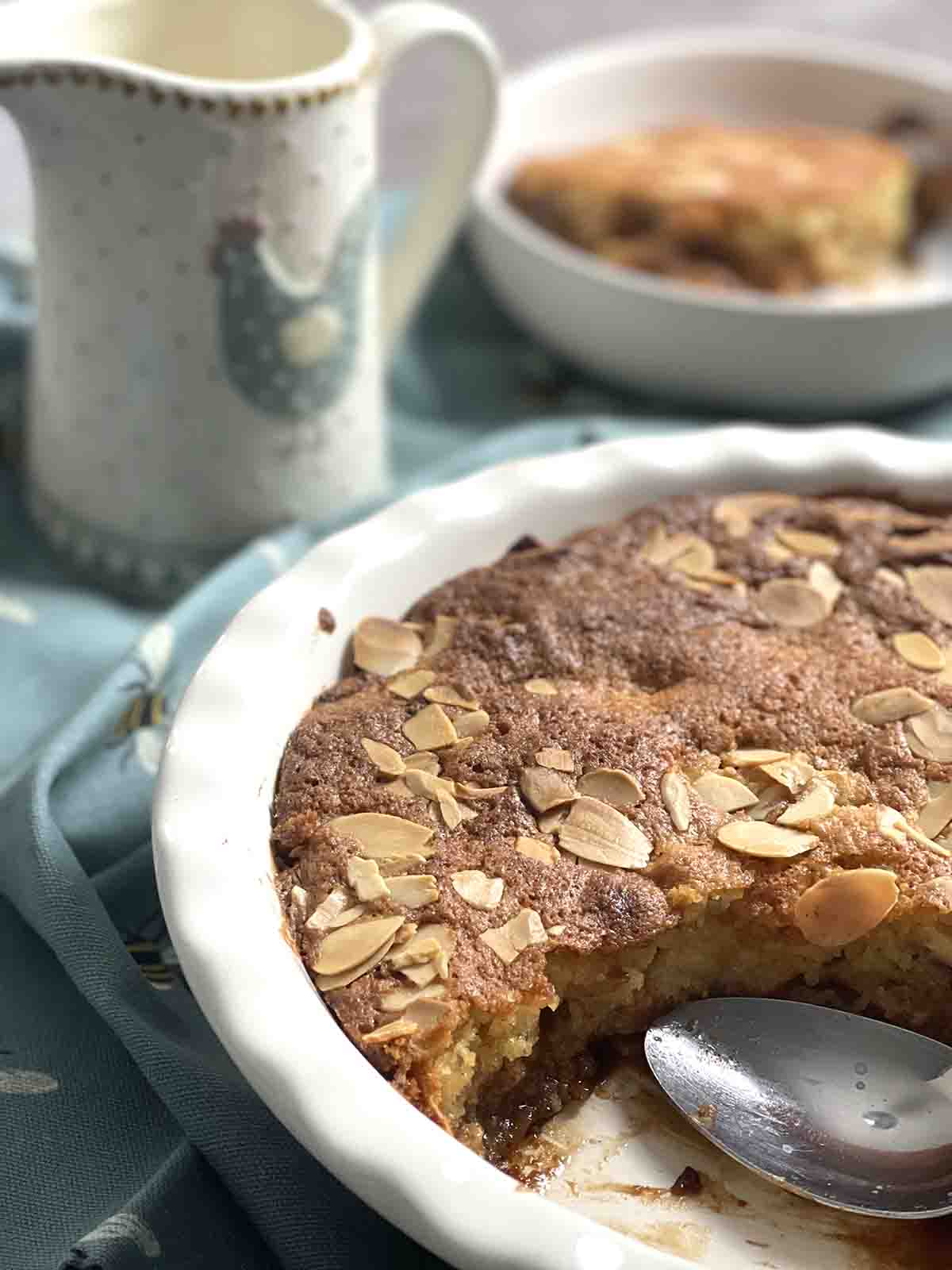apple sponge pudding with portion removed and in a bowl in the background.