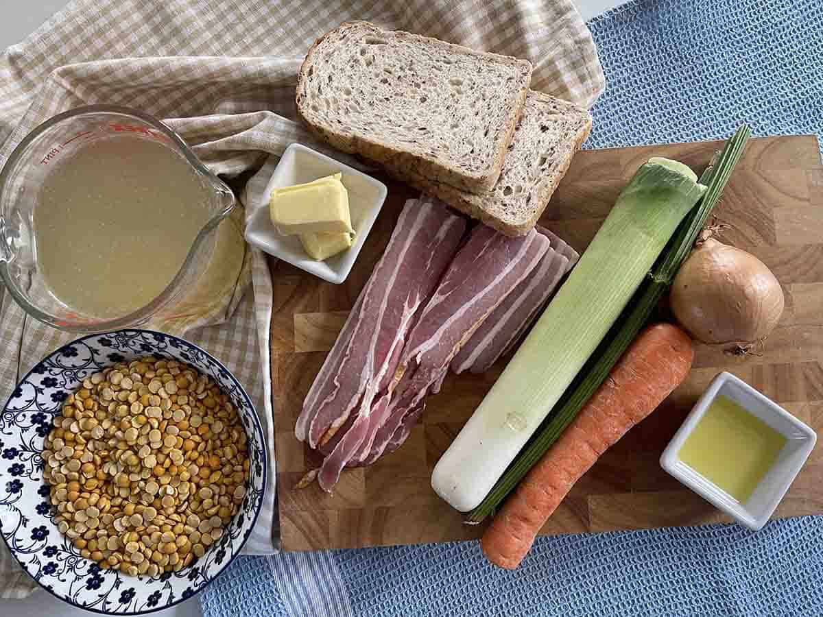 ingredients for the soup on a board including bacon, yellow split peas, leeks, onions, celery and carrots.