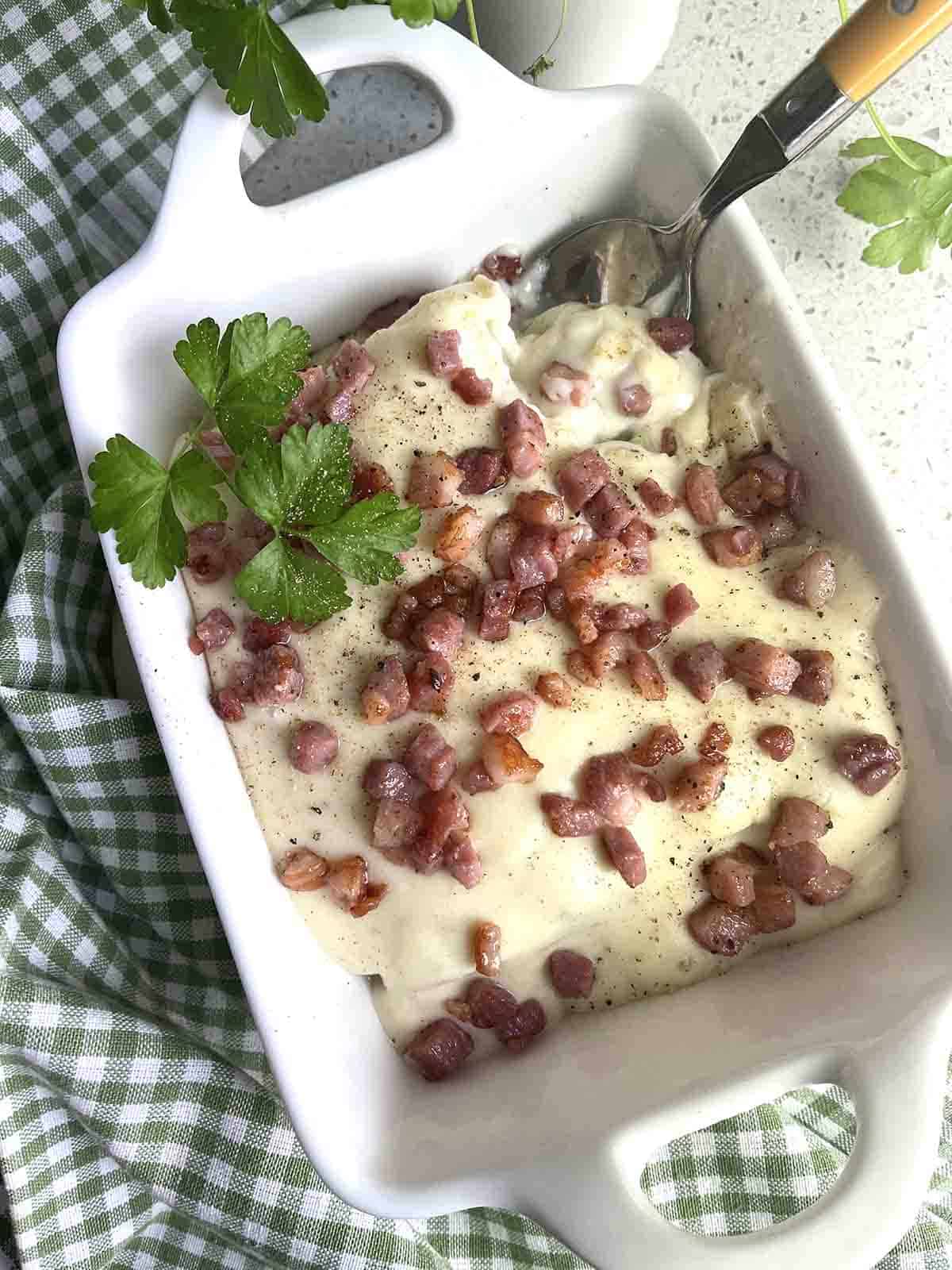 Leeks in white sauce with bacon pieces on top.