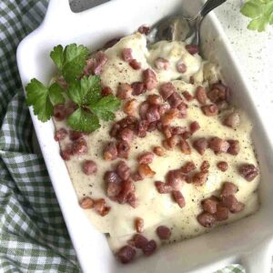 Leeks in white sauce with bacon pieces on top.