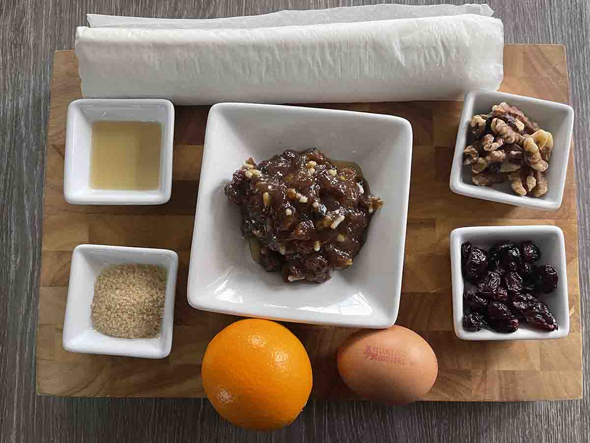 ingredients on a board including puff pastry, grandy, orange, walnuts, cranberries and mincemeat.