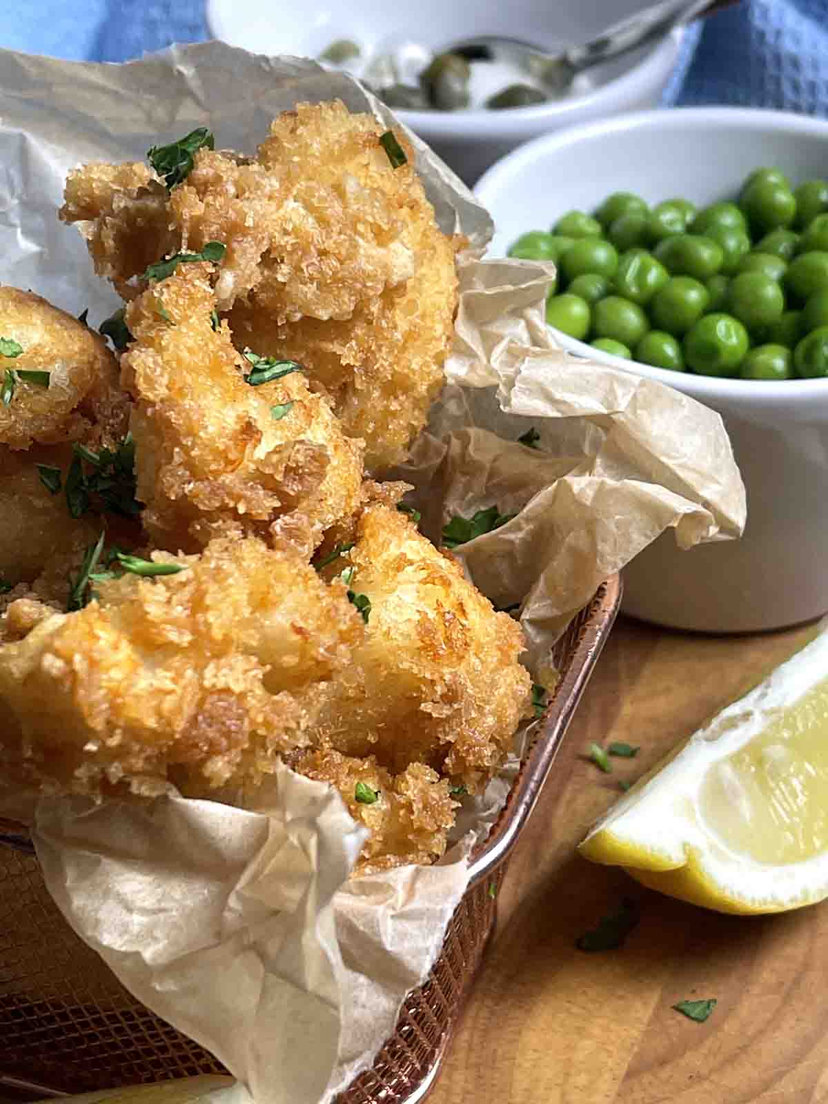 cod cheeks in panko in a wire dish with peas and lemon to the side.