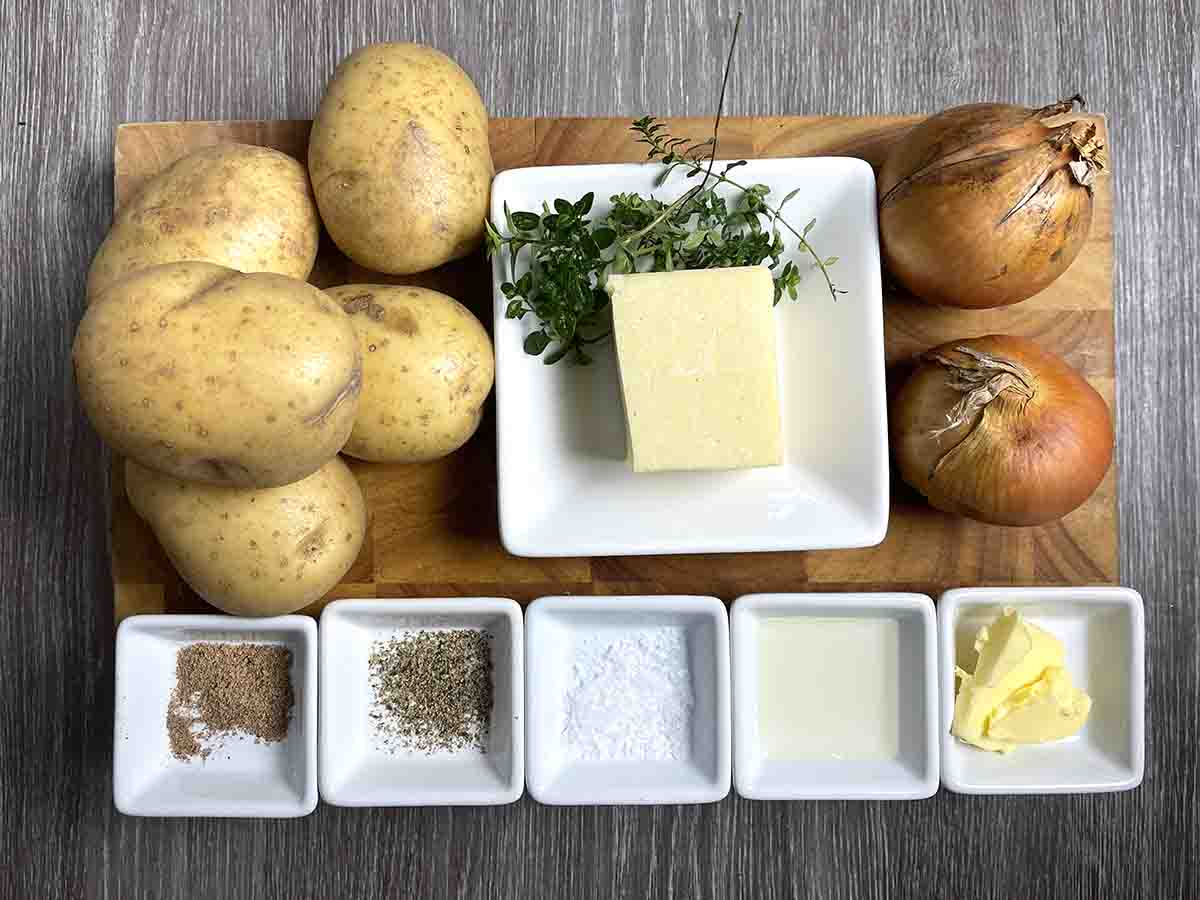 ingredients on a board including potatoes, onions, butter, cheese, nutmeg and seasoning.