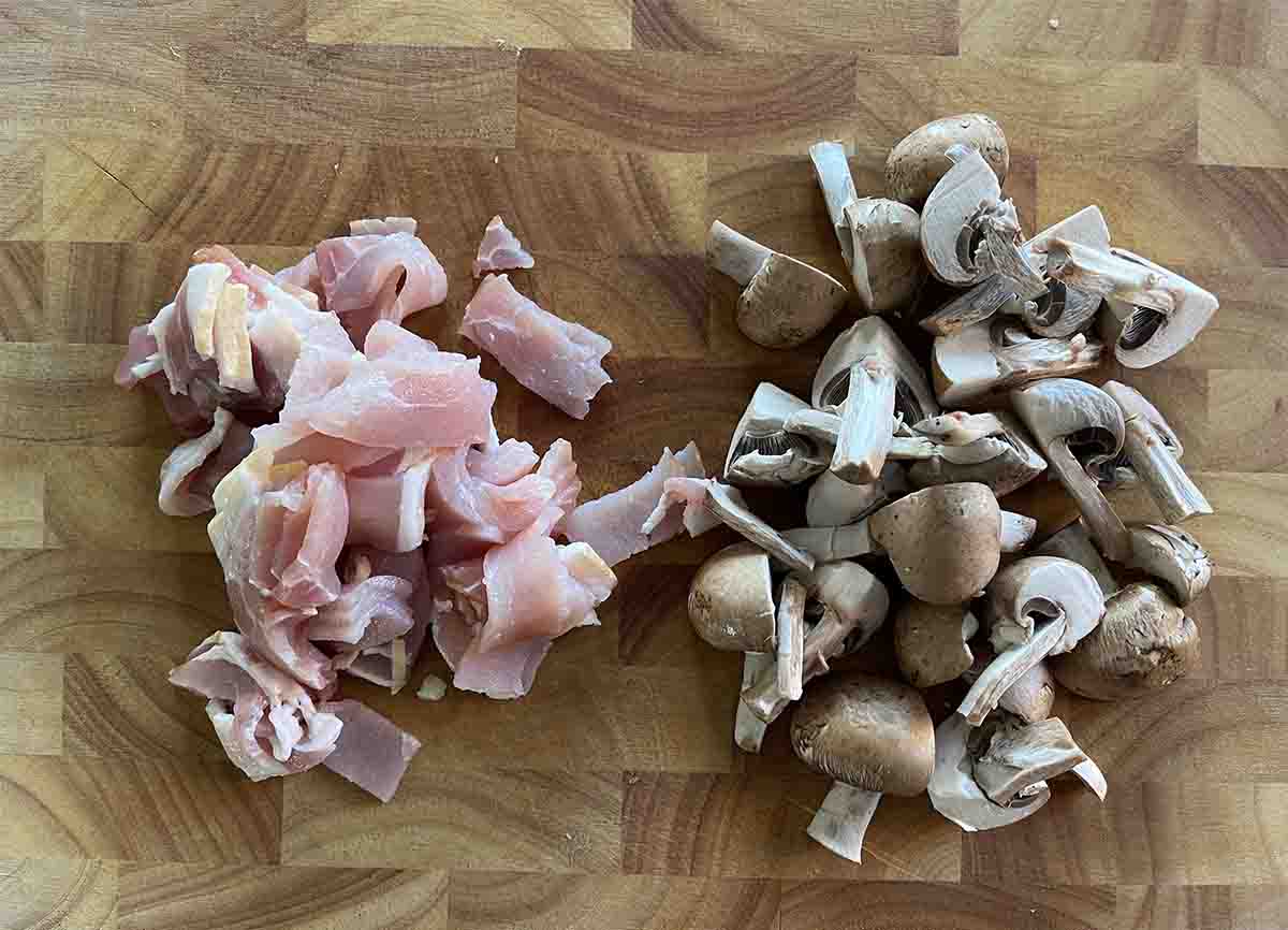 quartered mushrooms and sliced bacon on a board.