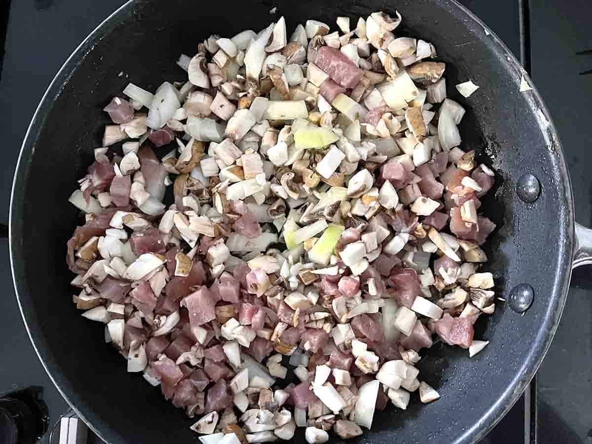 chopped onions, mushrooms and lardons in a pan.