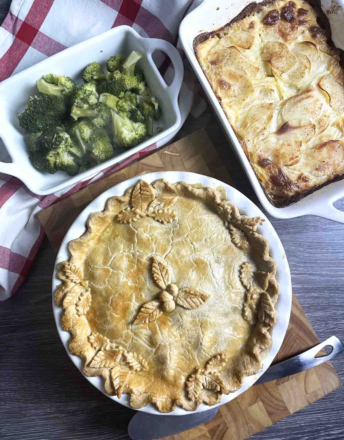 turkey and ham pie with dish of broccoli and potatoes at the top.