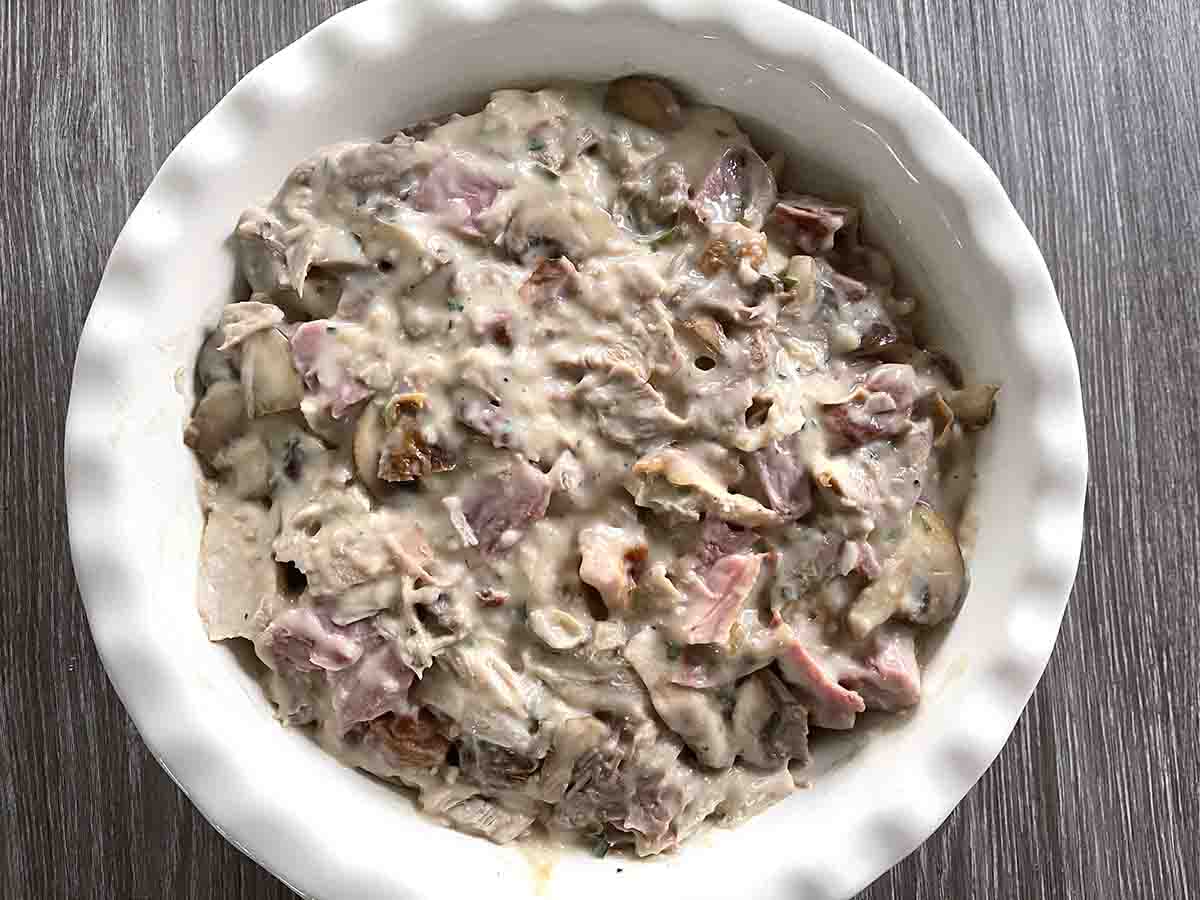 pie dish with ham turkey and sauce mixed together.