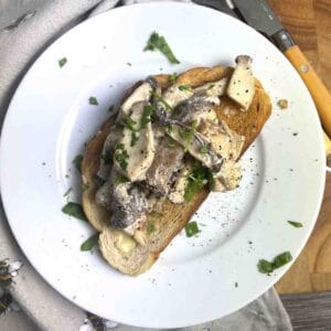 Creamy mushrooms on toast on a white plate with cutlery to the side.s