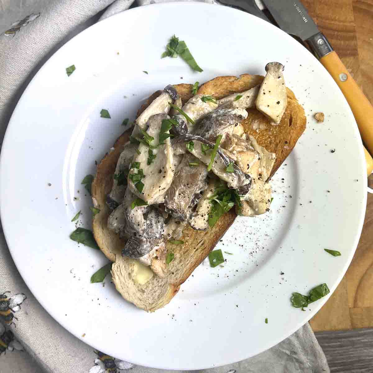 Creamy mushrooms on toast on a white plate with cutlery to the side.s