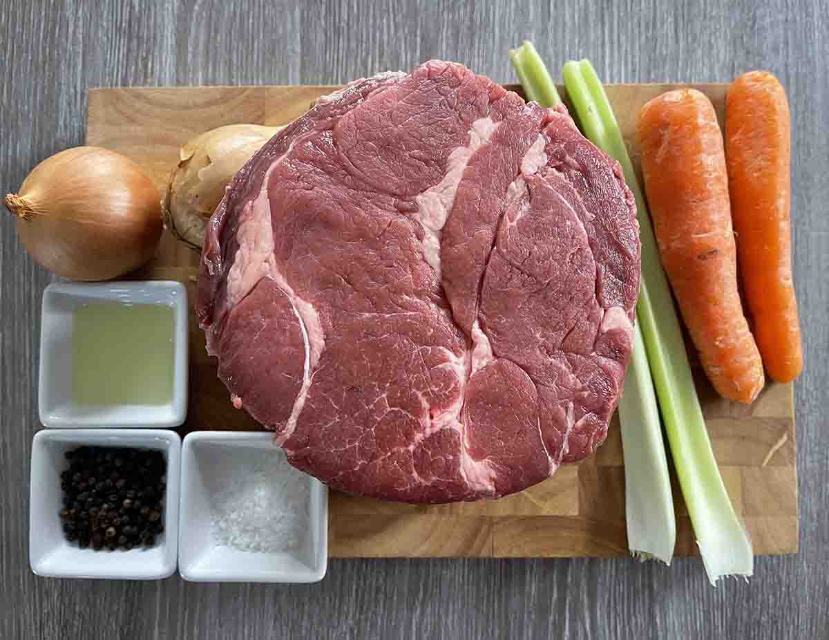 ingredients on a board including celery, carrots, onions, boneless rib of beef, oil, salt and black peppercorns.