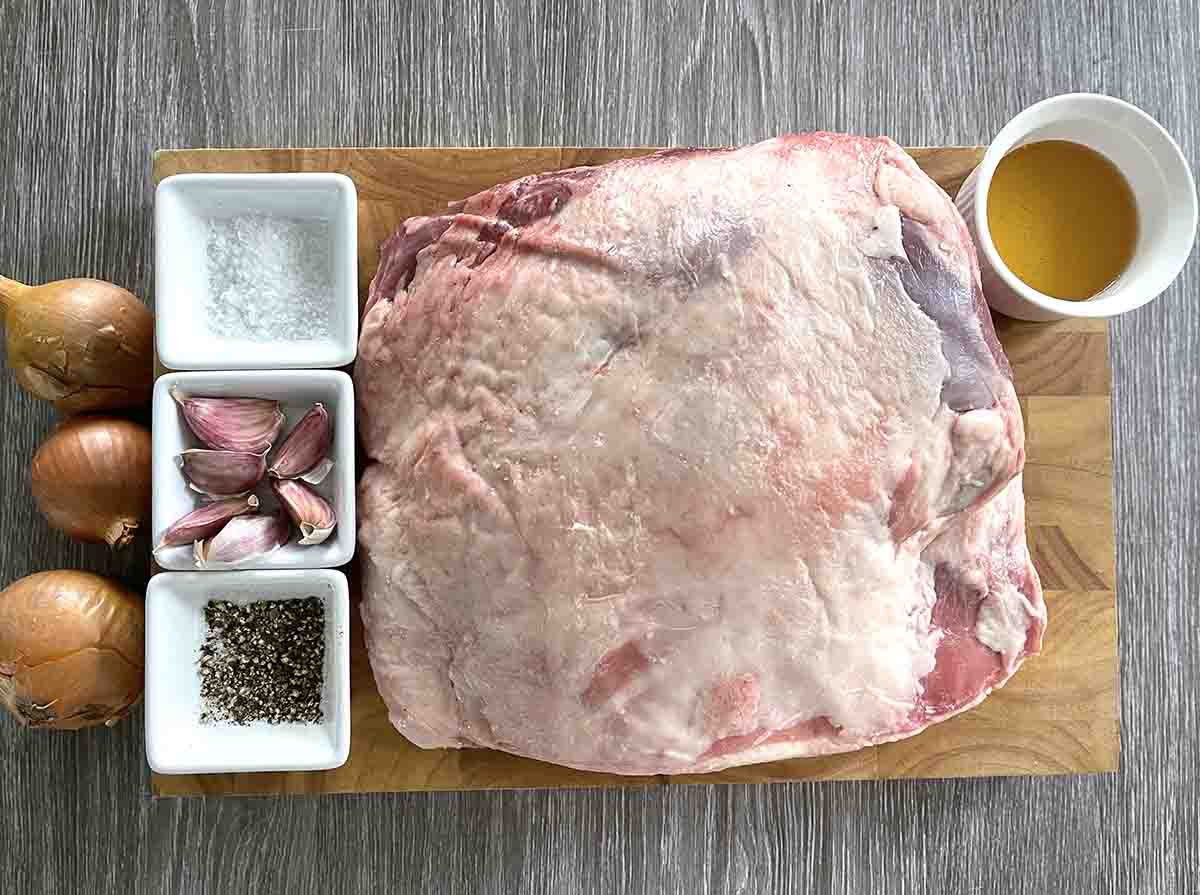 ingredients on a board including lamb shoulder, honey, garlic, seasoning, oil and onions.