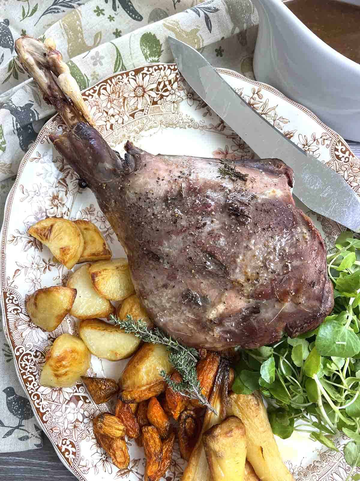 roast venison haunch on a plate with vegetables.