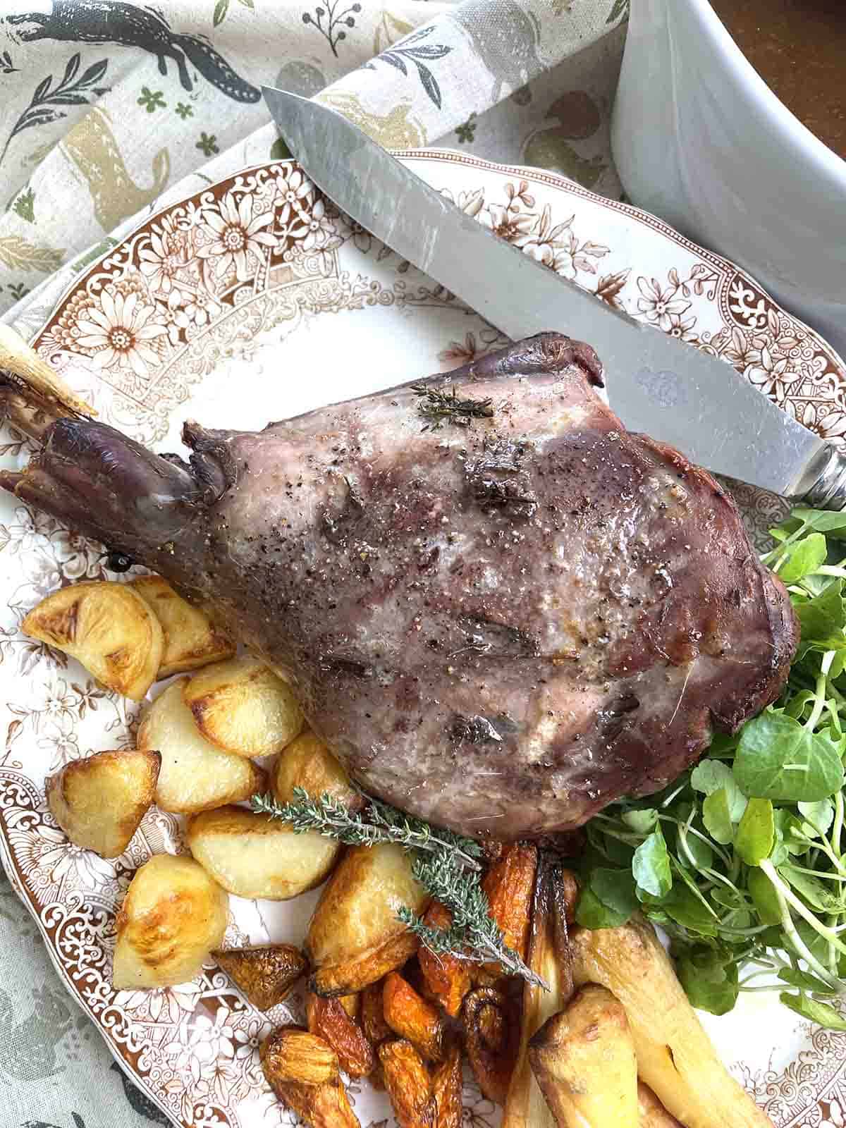 roast venison haunch on a plate with vegetables.