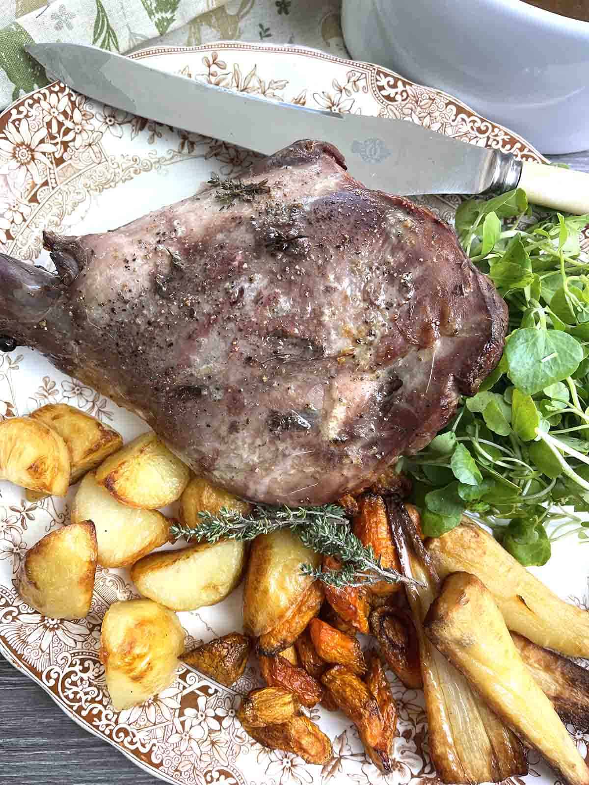 roast venison haunch on a plate with vegetables.