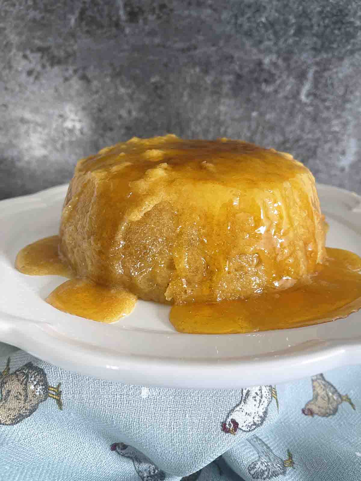 microwave sponge pudding on a plate with syrup falling down the sides.