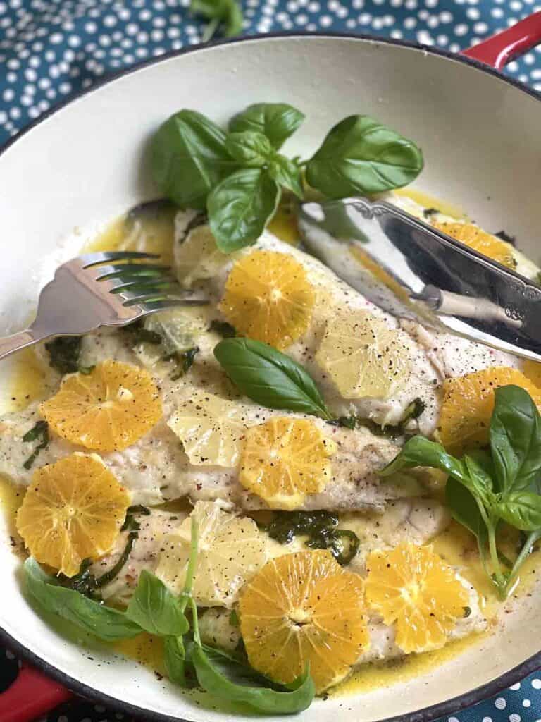 close up of cooked fish with citrus in a pan.