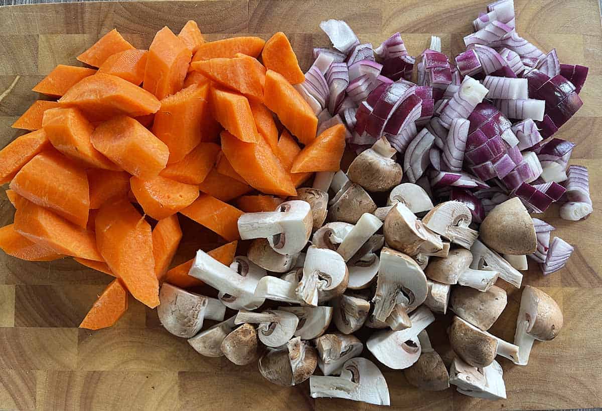 chpped carrots, mushrooms and onions on a board.
