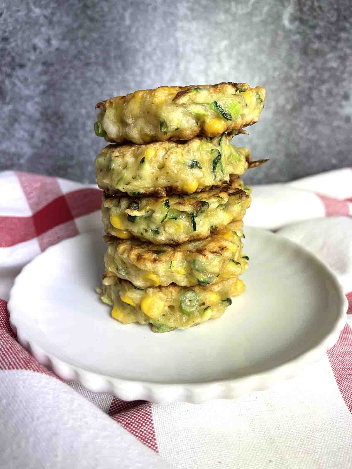 courgette nd sweetcorn fritters stacked on a plate.