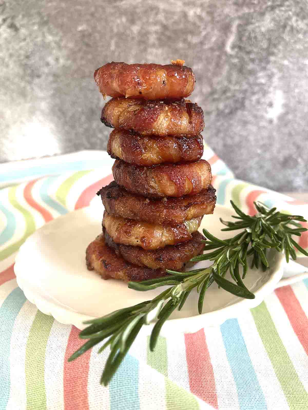 Bacon wrapped onion rings stacked on a plate.