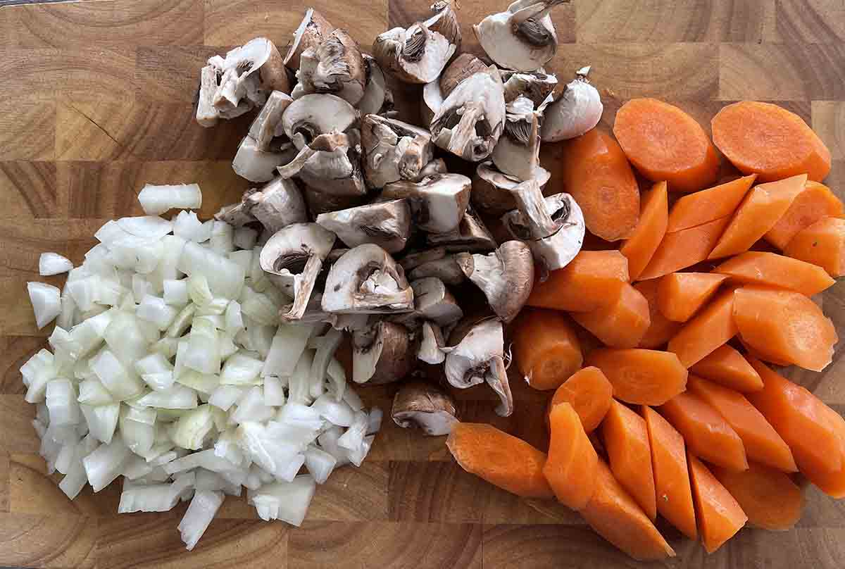 chopped onions, carrots and mushrooms on a board.