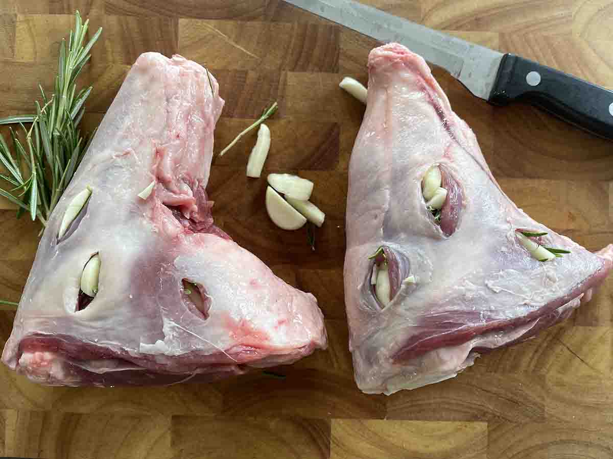 lamb shanks on a board studded with garlic and rosemary.