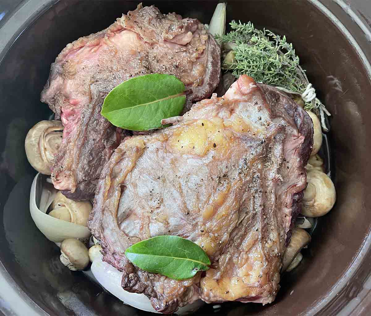 meat, herbs and stock added to the slow cooker.
