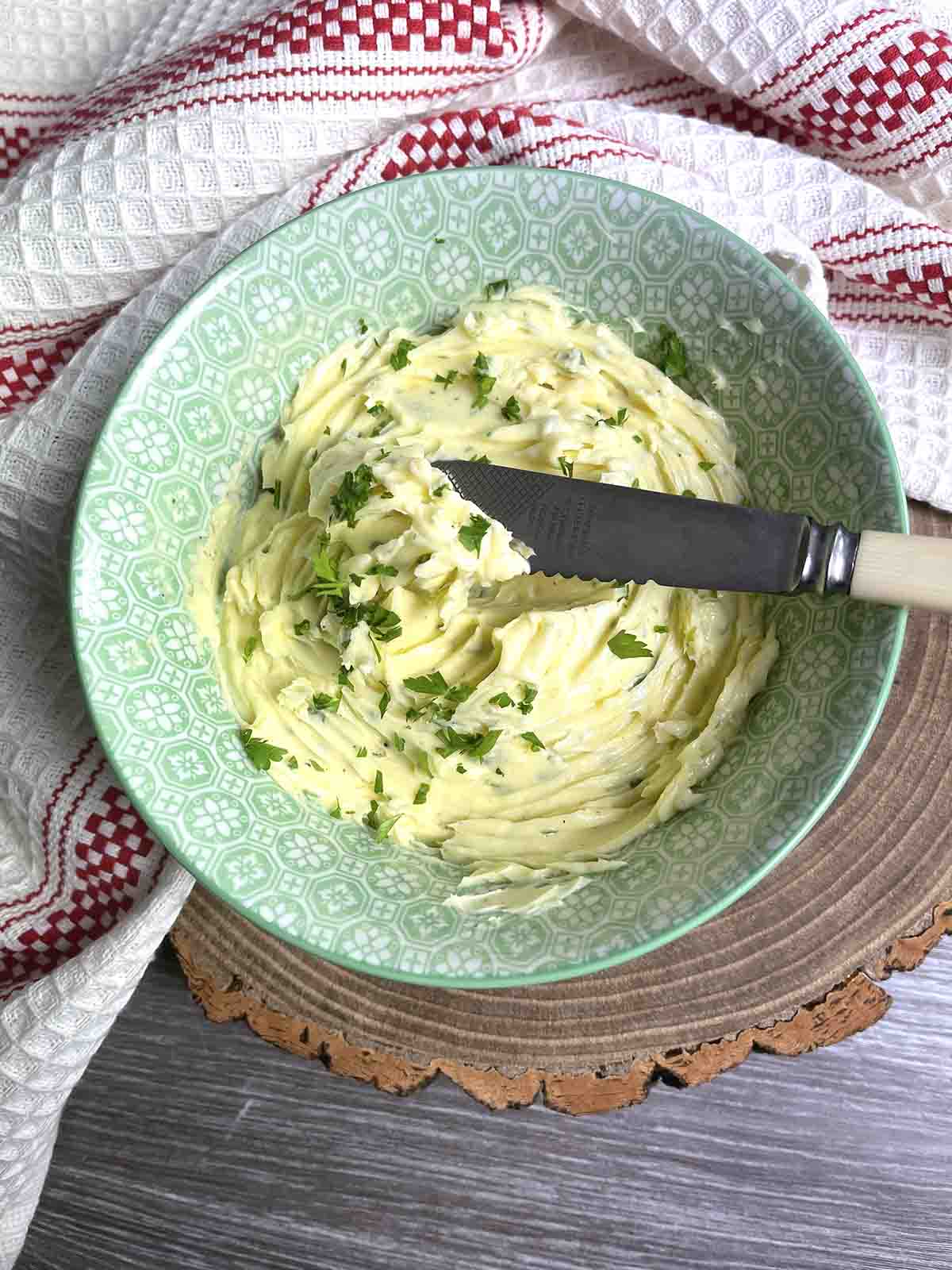 roasted garlic and herb butter in a bowl with a knife.