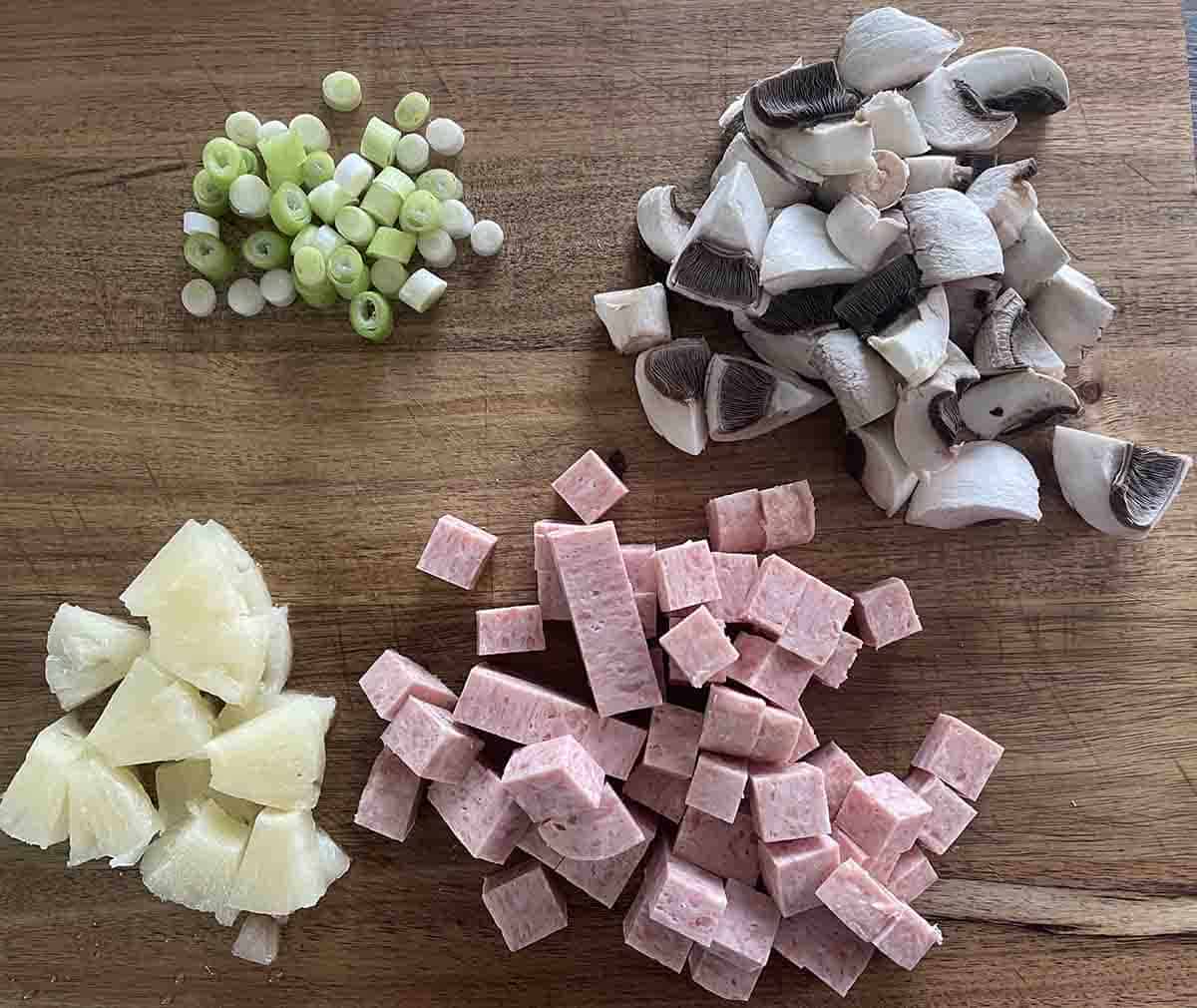chopped pineapple, mushrooms, spam and spring onions on a board.