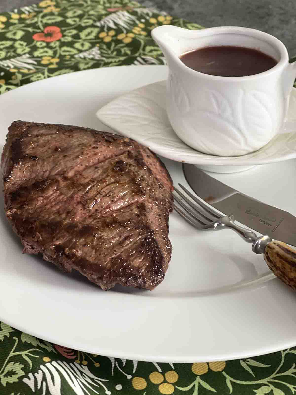 venison steak on a plate with a pot of redcurrant sauce.