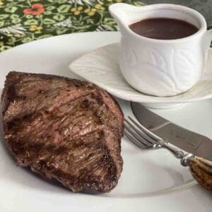 venison steak on a plate with a pot of redcurrant sauce.